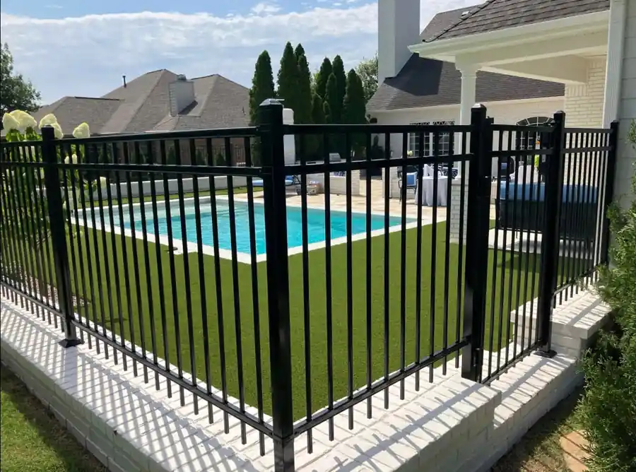 Black ornamental steel pool fence on a white brick knee wall around a backyard pool