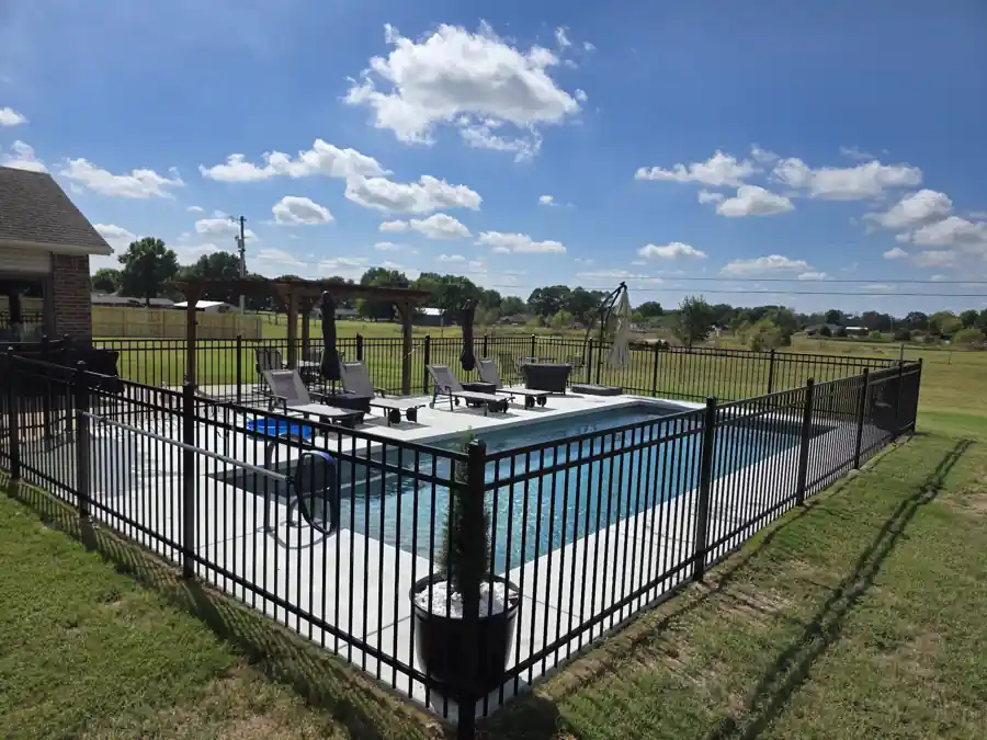Black ornamental steel fence around an in-ground pool and patio with open pasture beyond