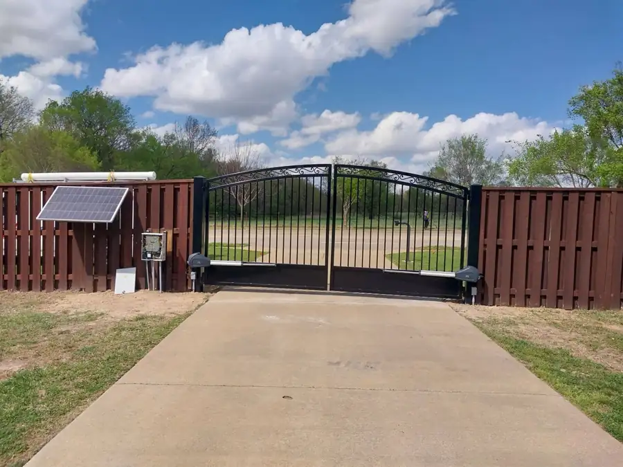 Arched black double drive gate with a solar panel and operator in a stained wood fence in Springdale