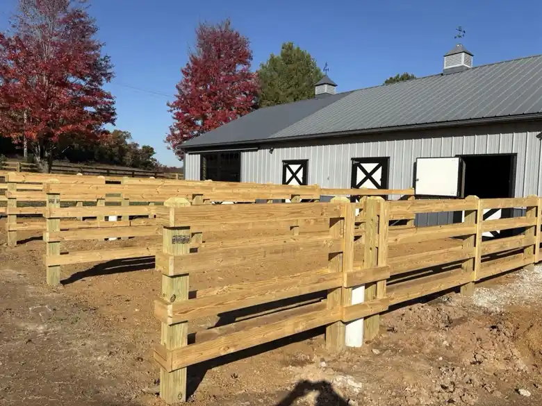 Four rail pine horse corral pens in front of a grey metal barn in Bentonville