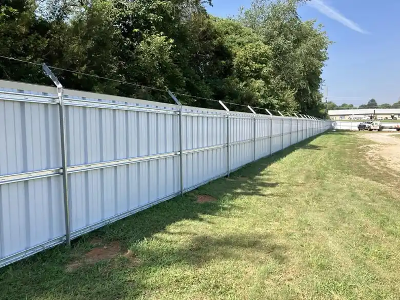 Long white R-panel steel security fence with barbed wire arms in Lowell