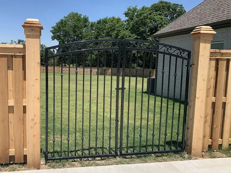 Arched black ornamental gate between capped cedar posts in Centerton