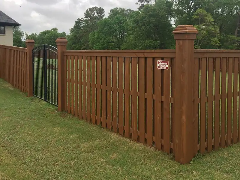 Stained cedar shadowbox fence with capped posts and an arched black steel gate in Bentonville