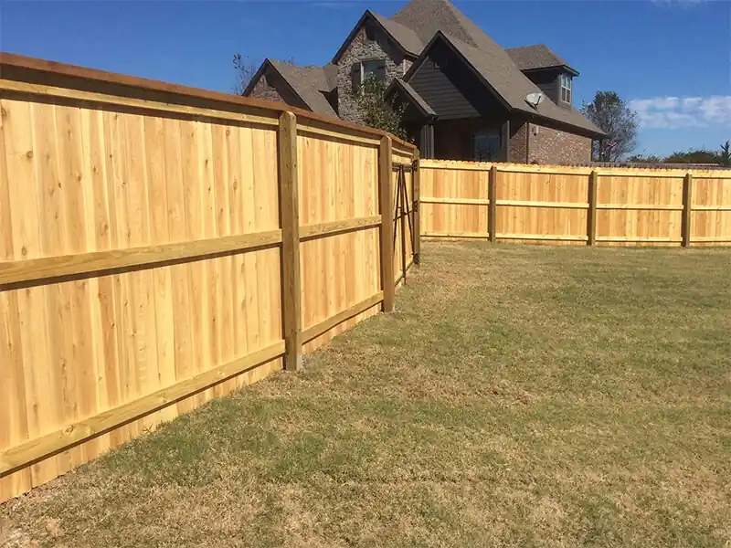 Tall cedar privacy fence with top trim across a large lawn in Cave Springs